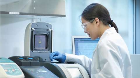 Laboratory technician stands at sample analysis machine monitoring progress